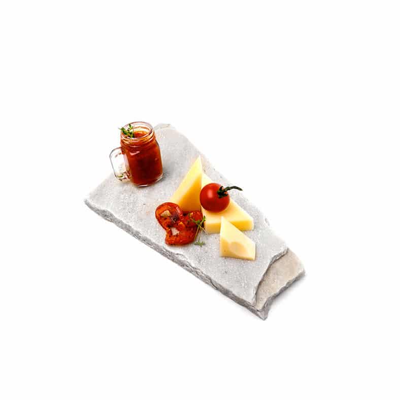 Käsewürfel und Tomaten neben Glas mit rotem Sirup auf Steinbrett.