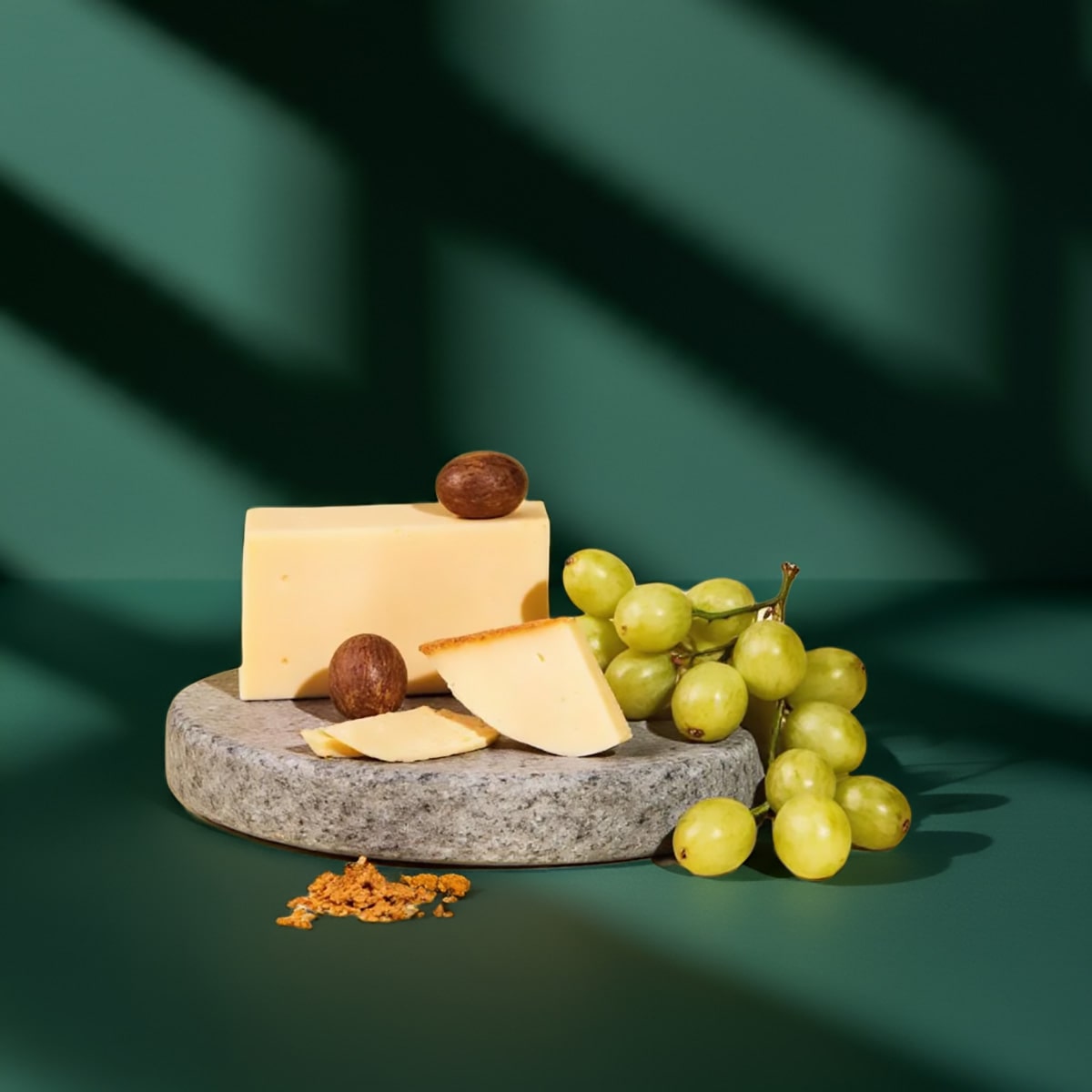 Käsestücke auf Steintablett mit Trauben, Nüssen und Brotcrackern vor grünem Hintergrund.