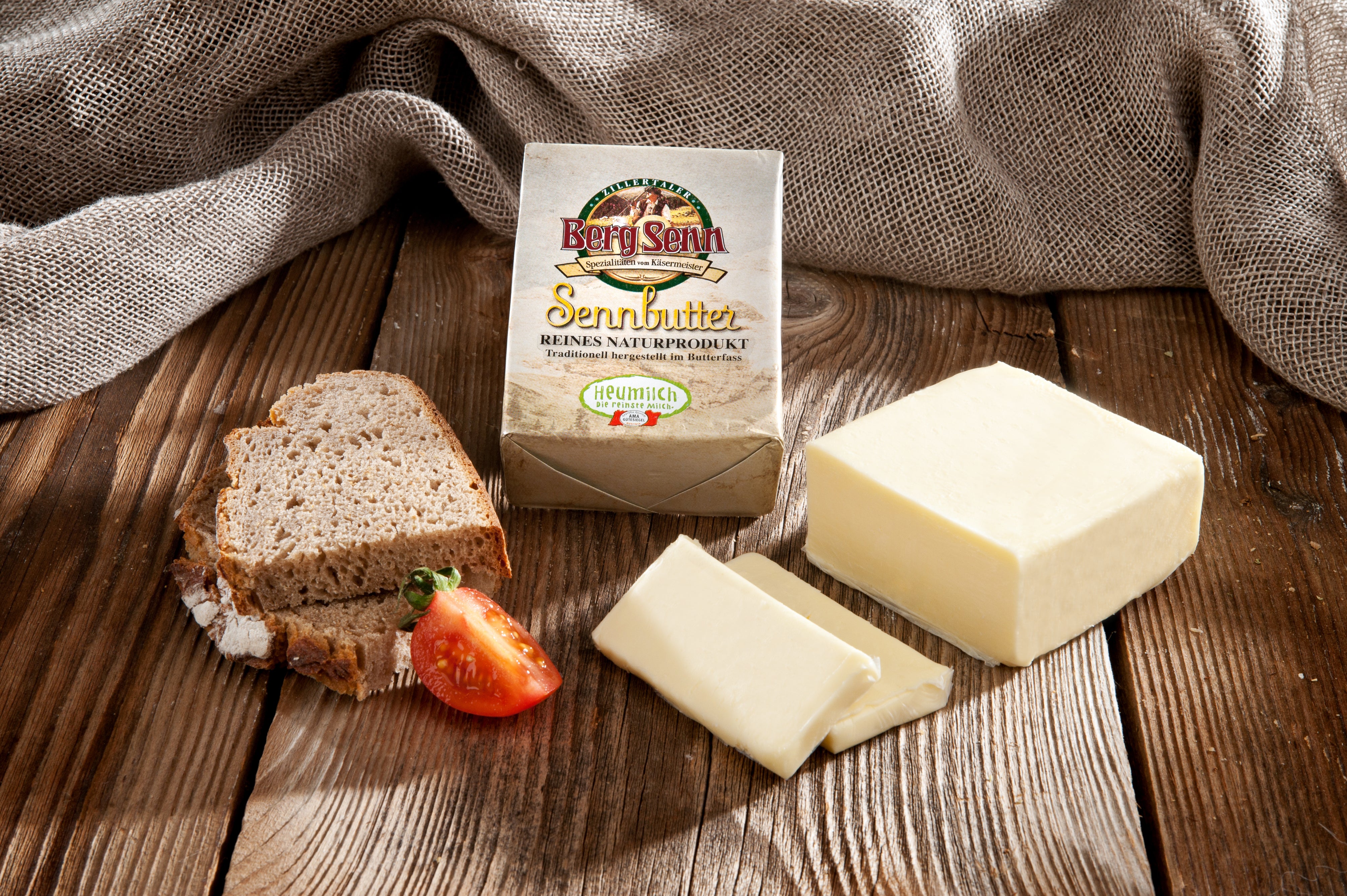 Sennbutter-Verpackung mit Butterstücken, Brotscheibe und Erdbeere auf Holzbrett