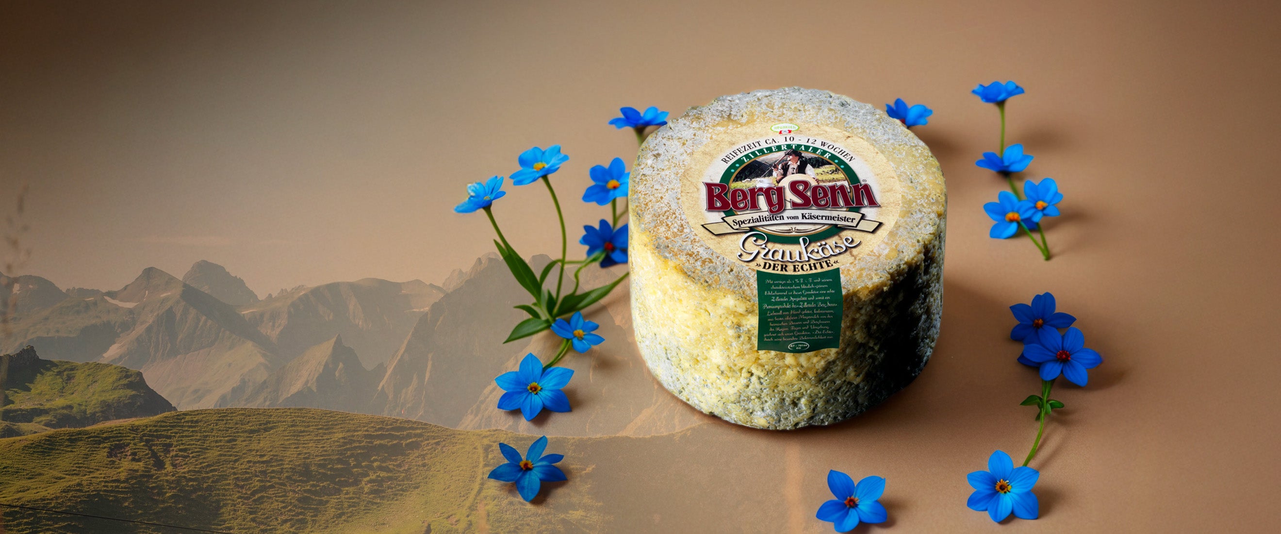 Bergkäse mit Label und Blüten vor Almlandschaft