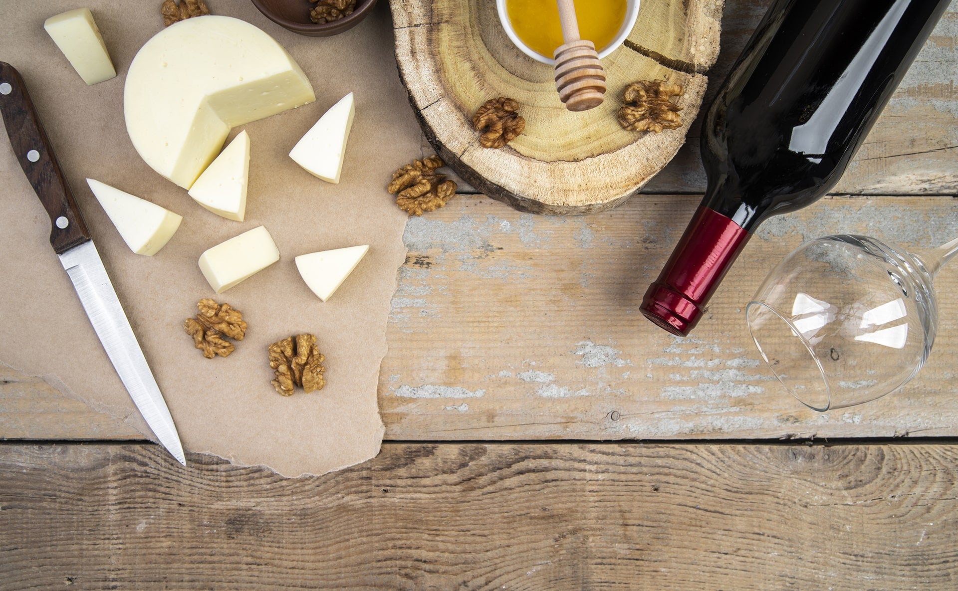 Käse in Schnittportionen mit Honig, Nüssen, Wein und Glas auf Holzbrett