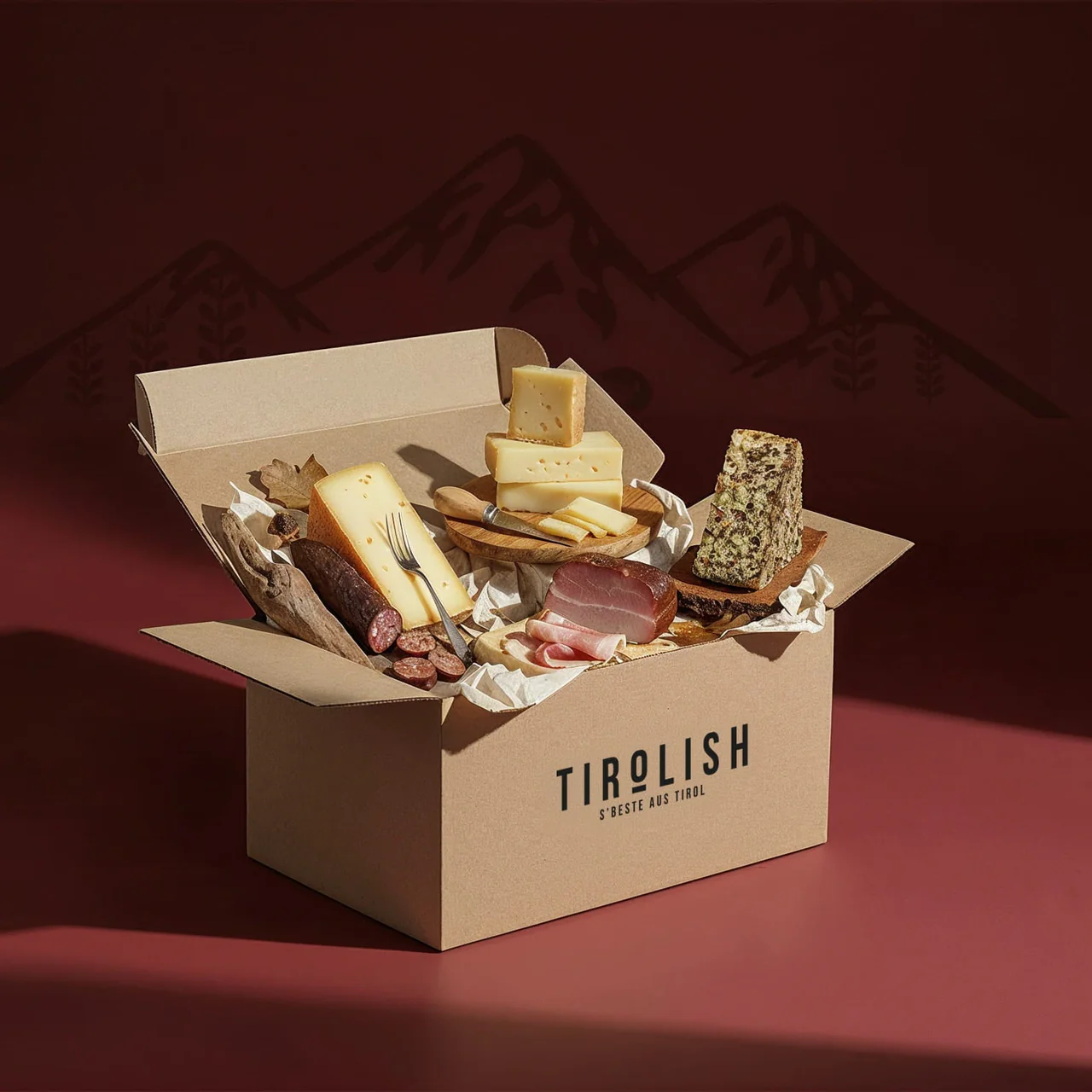 Geöffnete Kartonbox mit Tiroler Spezialitäten: Käse, Speck, Wurst und Brot auf Papier angerichtet.