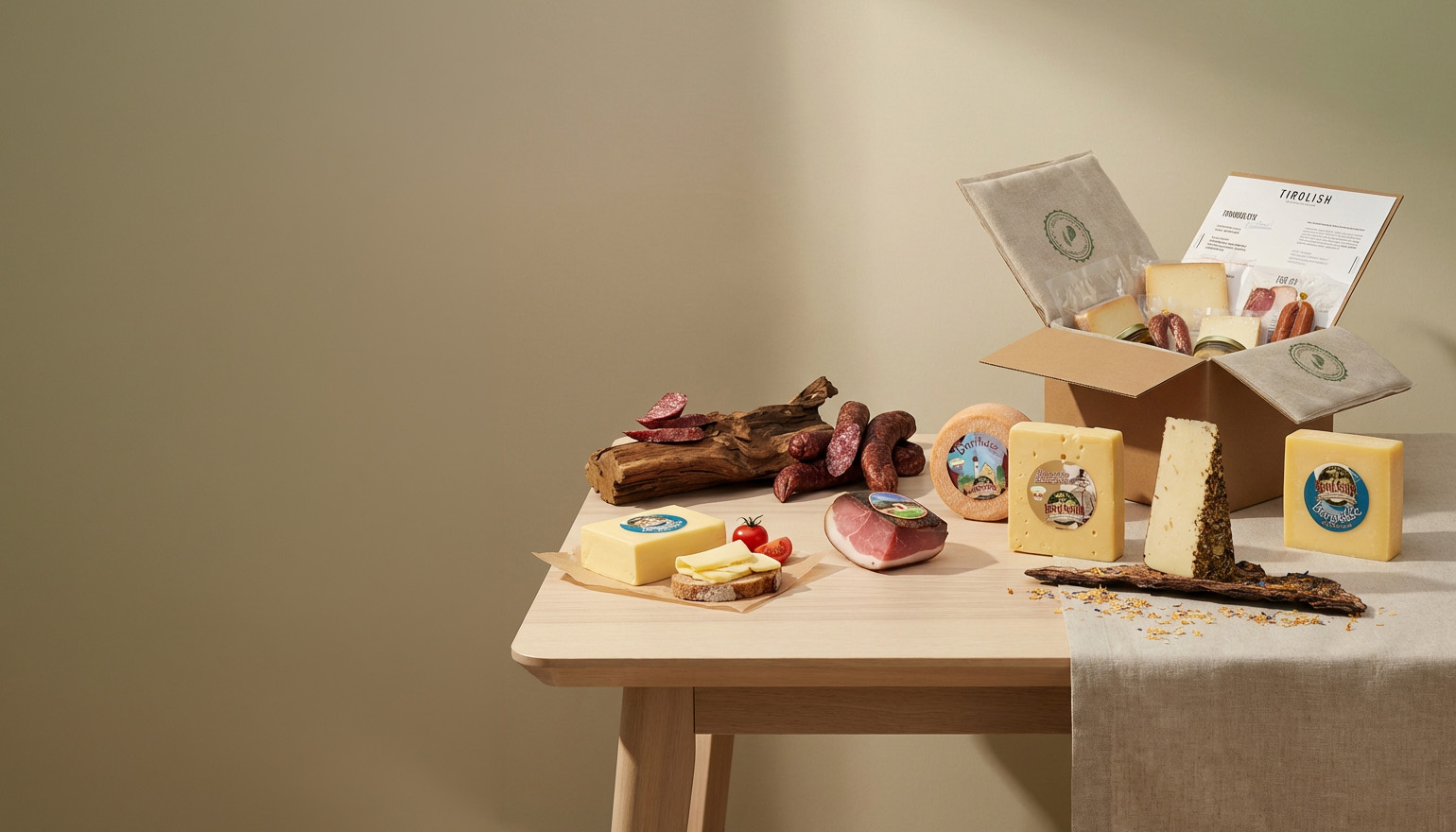 Tiroler Spezialitäten auf Holztisch mit Käsesorten, Speck und Wurst sowie geöffneter Produktbox.